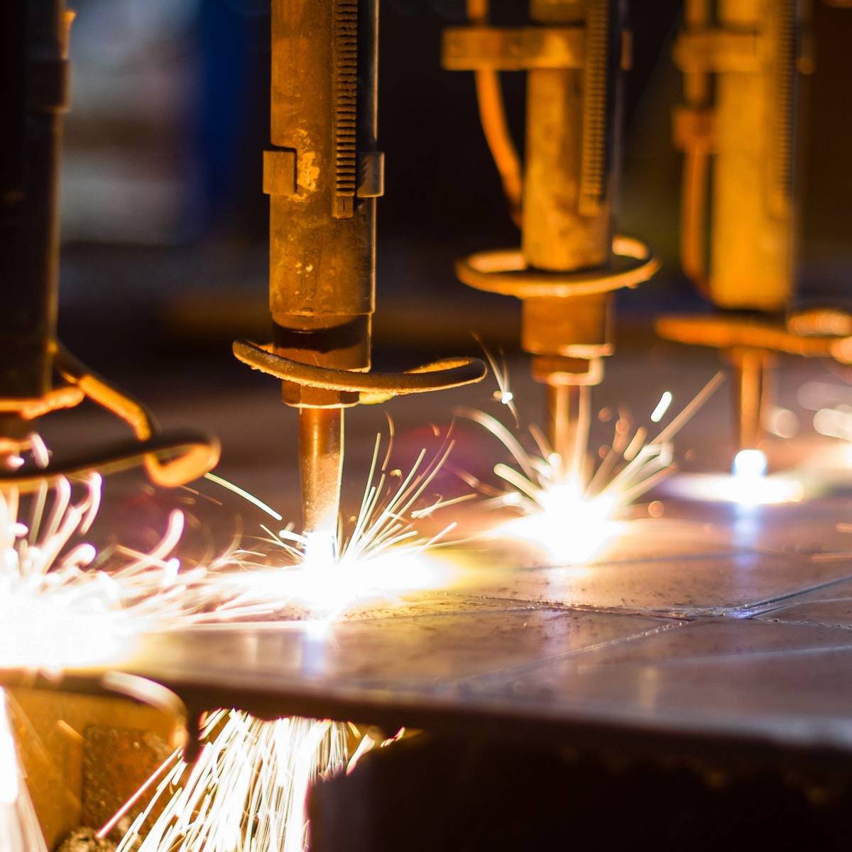 Welder sparks bright light while working on metal frame in a dark workshop.