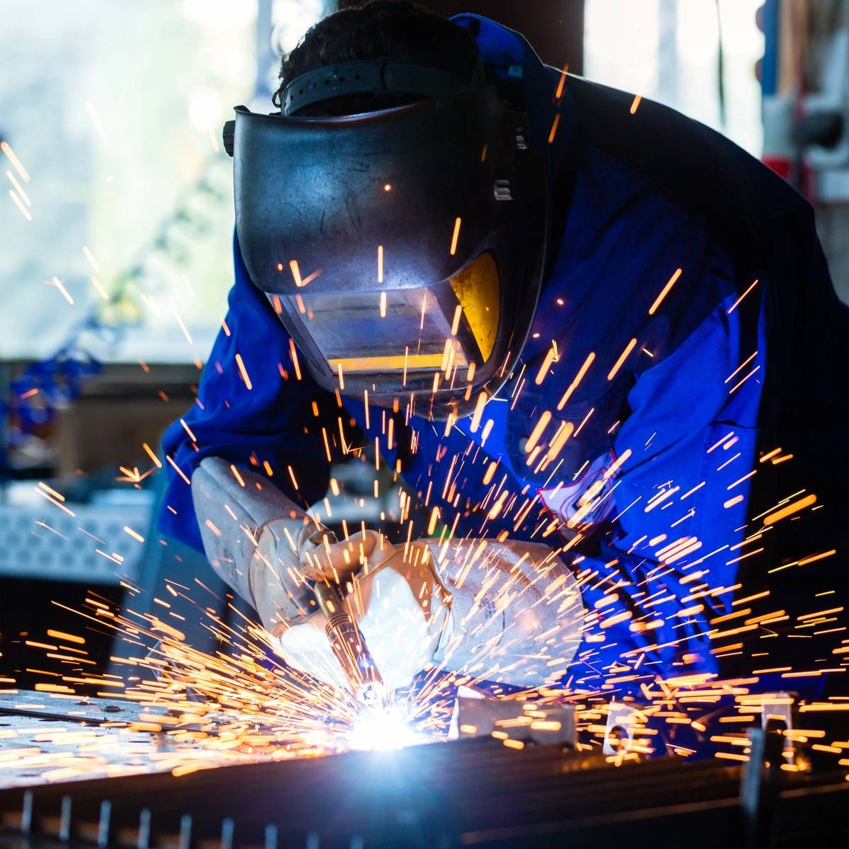 Welder sparks bright light while working on metal frame in a dark workshop.