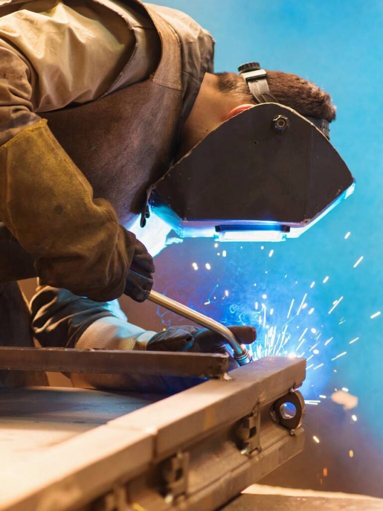 A welder in protective gear sparks bright blue light while working.