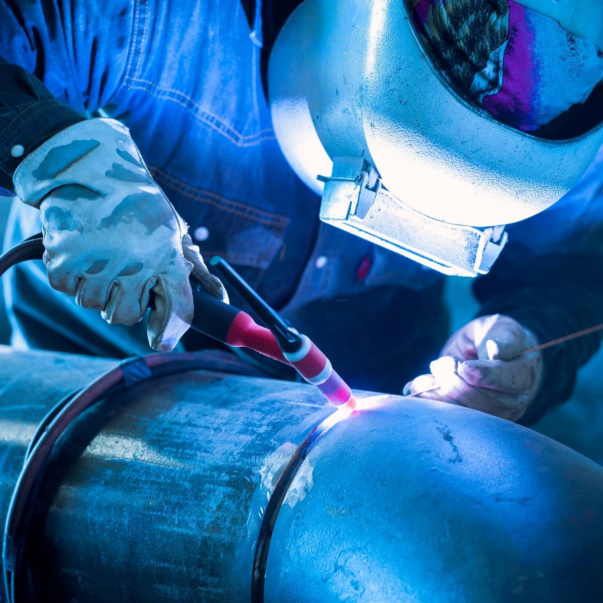 A welder in protective gear sparks bright blue light while working.