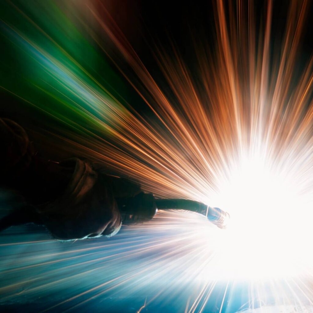 A welder in protective gear sparks bright blue light while working.