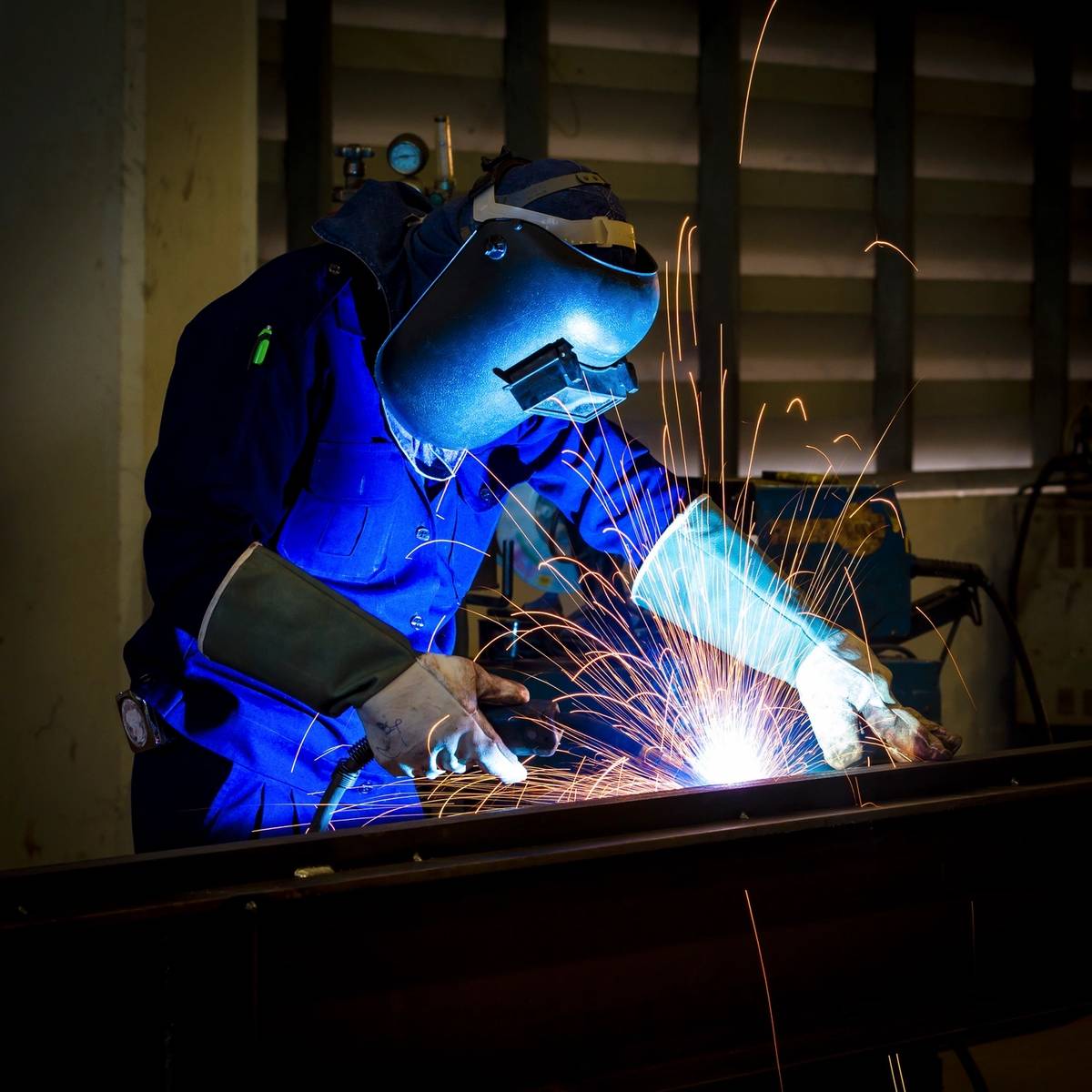 A welder in protective gear sparks bright blue light while working.