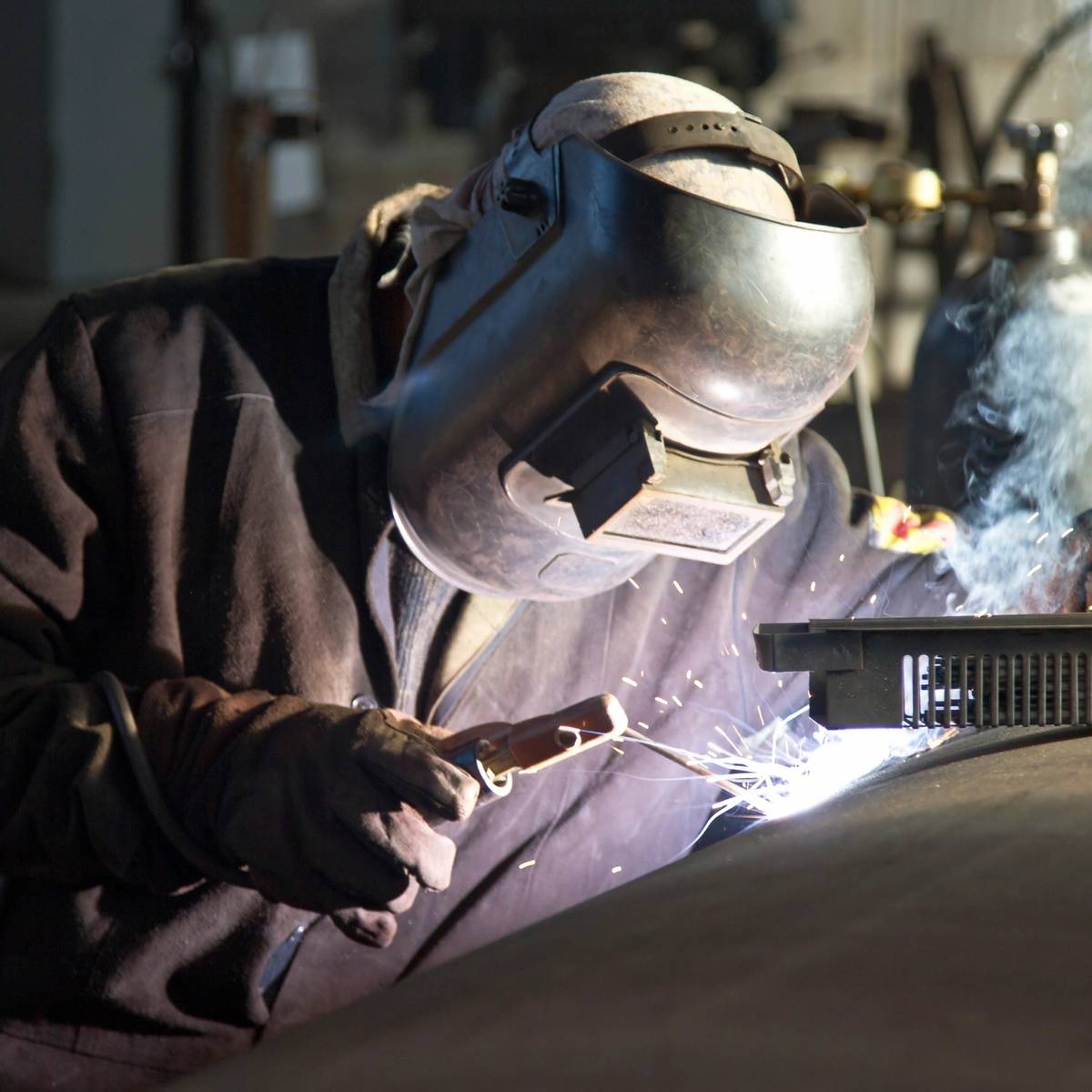 A welder in protective gear sparks bright blue light while working.