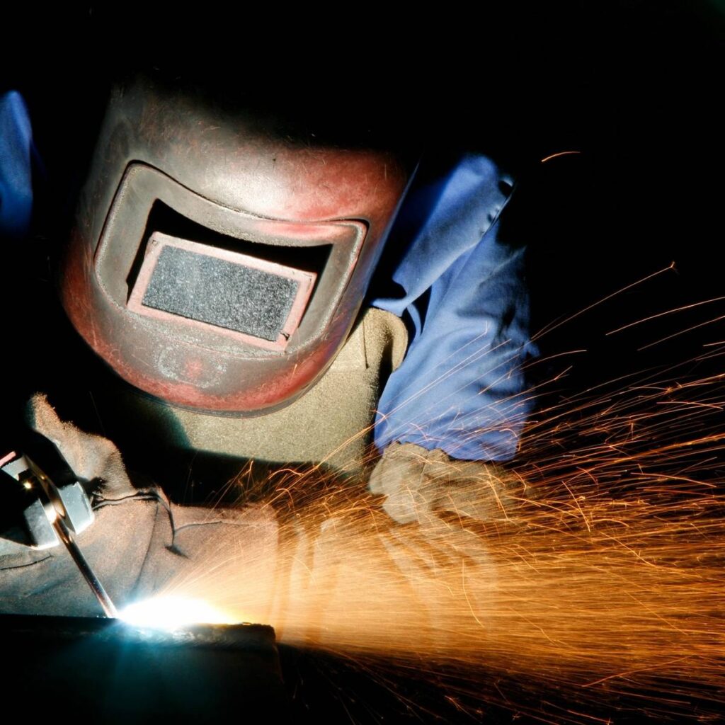 A welder in protective gear sparks bright blue light while working.
