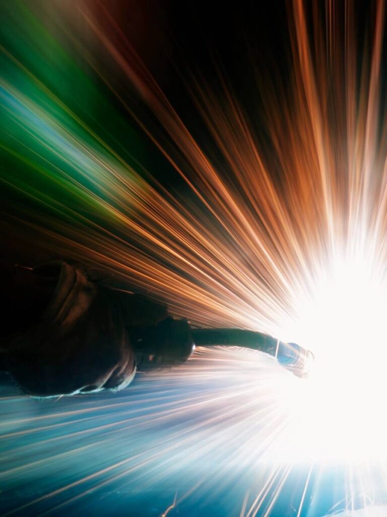 A welder in protective gear sparks bright blue light while working.