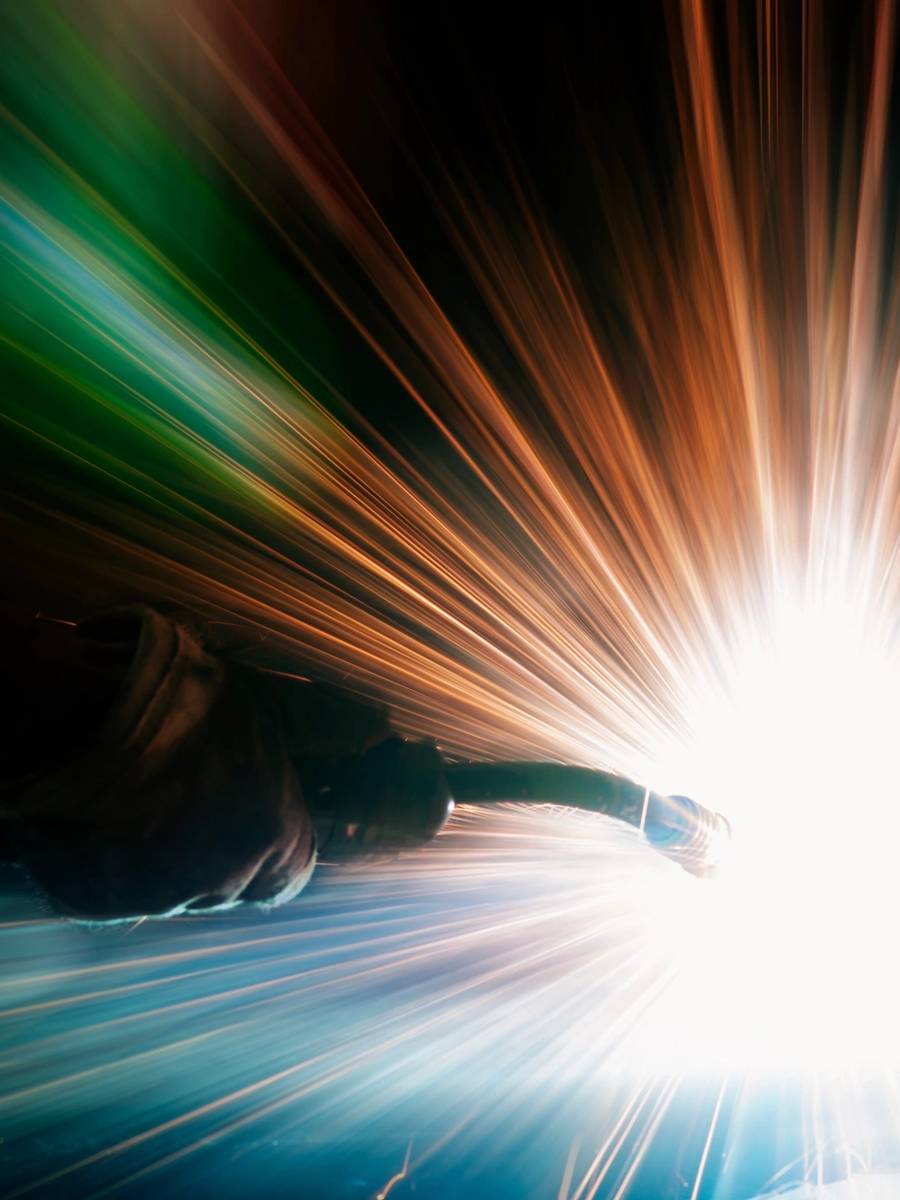 A welder in protective gear sparks bright blue light while working.