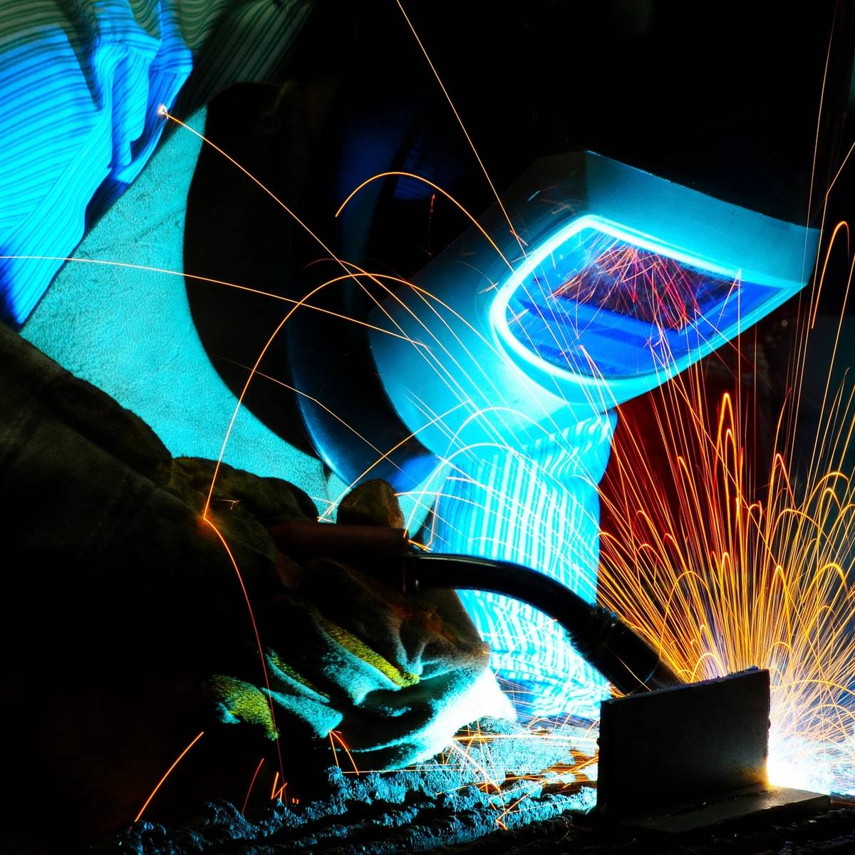 A welder in protective gear sparks bright blue light while working.